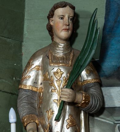 Zdjęcie nr 1: Rzeźba drążona, ścięta z tyłu. Figura zwrócona na wprost, w lewej, ugiętej ręce trzyma palmę męczeństwa, prawą, opuszczoną w dół podtrzymuje ruszt. Twarz podłużna, o młodzieńczych rysach, małych oczach i nosie, dużych ustach. Włosy krótkie, brązowe, w postaci loków opadają na tył głowy. Święty jest ubrany w szarą albę, srebrzoną u dołu z rękawami ze złotą lamówką, srebrny humerał oraz srebrzoną dalmatykę dekorowaną złoconymi kwiatami. Polichromia naturalistyczna w partiach ciała, palma zielona, ruszt czarny.