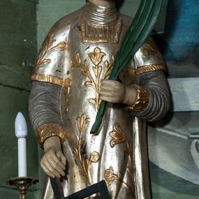 Zdjęcie nr 1: Rzeźba drążona, ścięta z tyłu. Figura zwrócona na wprost, w lewej, ugiętej ręce trzyma palmę męczeństwa, prawą, opuszczoną w dół podtrzymuje ruszt. Twarz podłużna, o młodzieńczych rysach, małych oczach i nosie, dużych ustach. Włosy krótkie, brązowe, w postaci loków opadają na tył głowy. Święty jest ubrany w szarą albę, srebrzoną u dołu z rękawami ze złotą lamówką, srebrny humerał oraz srebrzoną dalmatykę dekorowaną złoconymi kwiatami. Polichromia naturalistyczna w partiach ciała, palma zielona, ruszt czarny.