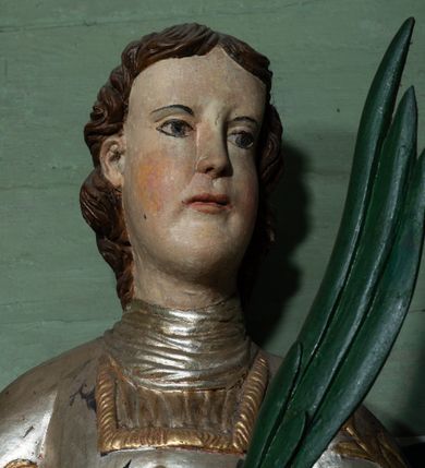 Zdjęcie nr 2: Rzeźba drążona, ścięta z tyłu. Figura zwrócona na wprost, w lewej, ugiętej ręce trzyma palmę męczeństwa, prawą, opuszczoną w dół podtrzymuje ruszt. Twarz podłużna, o młodzieńczych rysach, małych oczach i nosie, dużych ustach. Włosy krótkie, brązowe, w postaci loków opadają na tył głowy. Święty jest ubrany w szarą albę, srebrzoną u dołu z rękawami ze złotą lamówką, srebrny humerał oraz srebrzoną dalmatykę dekorowaną złoconymi kwiatami. Polichromia naturalistyczna w partiach ciała, palma zielona, ruszt czarny.