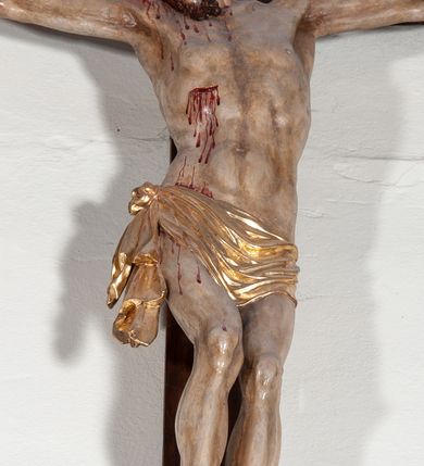 Zdjęcie nr 3: Chrystus rozpięty na krzyżu z ułożonymi niemal poziomo, szeroko rozłożonymi rękami, z ugiętą w kolanie prawą nogą, lewą niemal wyprostowaną, stopami założonymi prawa na lewą i przebitymi jednym gwoździem, z głową skłonioną na prawy bark. Twarz pociągła, z długim nosem i wpółotwartymi ustami, okolona zarostem i długimi spływającymi na kark włosami, spod których widać lewe ucho. Budowa anatomiczna i muskulatura silnie podkreślona naprężeniem ciała. Karnacja w odcieniu naturalnym z zaznaczonymi śladami męki. Rana w prawym boku. Wokół bioder perizonium zawiązane na prawym koku w węzeł, ze zwisem tkaniny przy prawym udzie. Nad głową Chrystusa poziomo ułożony titulus z końcami wyciętym w jaskółczy ogon, z literami INRI. Krzyż malowany na kolor brązowy, karnacja i włosy Chrystusa w kolorze naturalnym, perizonium srebrzone i złocone, titulus biały ze złoconymi krawędziami.
