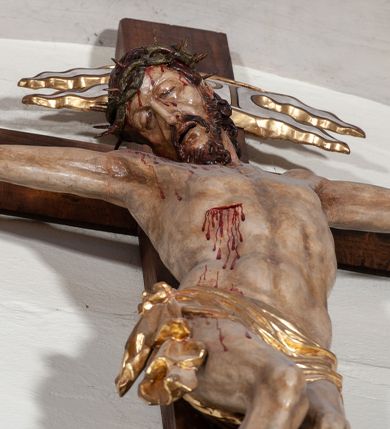 Zdjęcie nr 2: Chrystus rozpięty na krzyżu z ułożonymi niemal poziomo, szeroko rozłożonymi rękami, z ugiętą w kolanie prawą nogą, lewą niemal wyprostowaną, stopami założonymi prawa na lewą i przebitymi jednym gwoździem, z głową skłonioną na prawy bark. Twarz pociągła, z długim nosem i wpółotwartymi ustami, okolona zarostem i długimi spływającymi na kark włosami, spod których widać lewe ucho. Budowa anatomiczna i muskulatura silnie podkreślona naprężeniem ciała. Karnacja w odcieniu naturalnym z zaznaczonymi śladami męki. Rana w prawym boku. Wokół bioder perizonium zawiązane na prawym koku w węzeł, ze zwisem tkaniny przy prawym udzie. Nad głową Chrystusa poziomo ułożony titulus z końcami wyciętym w jaskółczy ogon, z literami INRI. Krzyż malowany na kolor brązowy, karnacja i włosy Chrystusa w kolorze naturalnym, perizonium srebrzone i złocone, titulus biały ze złoconymi krawędziami.
