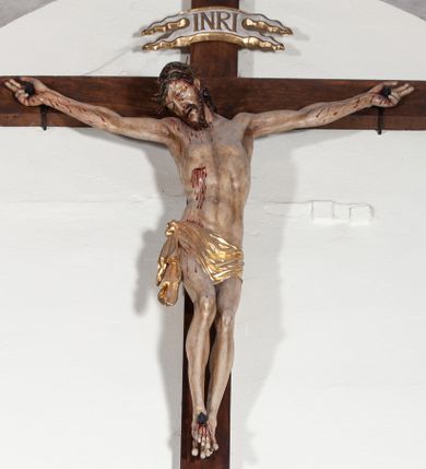 Zdjęcie nr 1: Chrystus rozpięty na krzyżu z ułożonymi niemal poziomo, szeroko rozłożonymi rękami, z ugiętą w kolanie prawą nogą, lewą niemal wyprostowaną, stopami założonymi prawa na lewą i przebitymi jednym gwoździem, z głową skłonioną na prawy bark. Twarz pociągła, z długim nosem i wpółotwartymi ustami, okolona zarostem i długimi spływającymi na kark włosami, spod których widać lewe ucho. Budowa anatomiczna i muskulatura silnie podkreślona naprężeniem ciała. Karnacja w odcieniu naturalnym z zaznaczonymi śladami męki. Rana w prawym boku. Wokół bioder perizonium zawiązane na prawym koku w węzeł, ze zwisem tkaniny przy prawym udzie. Nad głową Chrystusa poziomo ułożony titulus z końcami wyciętym w jaskółczy ogon, z literami INRI. Krzyż malowany na kolor brązowy, karnacja i włosy Chrystusa w kolorze naturalnym, perizonium srebrzone i złocone, titulus biały ze złoconymi krawędziami.
