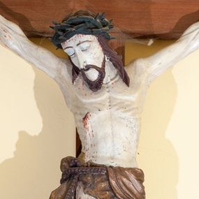 Zdjęcie nr 1: Chrystus rozpięty na krzyżu w lekkim zwisie ciała, z ukośnie ułożonymi rękami, z niemal wyprostowanymi nogami, stopami założonymi prawa na lewą i przebitymi jednym gwoździem, z głową przechyloną na prawy bark. Proporcje ciała zaburzone: duża głowa, krótki tors, chude ręce z drobnymi dłońmi, nogi muskularne z dużymi stopami. Twarz trójkątna, z zamkniętymi oczami, okolona krótkim zarostem i spływającymi na barki włosami. Na włosy nałożona korona cierniowa. Rana w prawym boku.  Wokół bioder podwiązane sznurem perizonium ze zwisem tkaniny przy prawym udzie. Nad głową Chrystusa ułożony poziomo titulus z wyciętymi w jaskółczy ogon końcami, z literami IN RI. Krzyż w kolorze brązowym, karnacja ciała blada, włosy ciemne, perizonium złocone (pociemniałe), titulus biały.