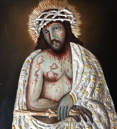 Zdjęcie nr 1: Obraz w kształcie stojącego prostokąta, w rzeźbionej złoconej ramie, na cokole, zdobionej uproszczonym motywem korony cierniowej, z rozetami w narożach. Przedstawienie w półpostaci Chrystusa w typie Ecce Homo, z głową lekko przechyloną na prawe ramię, z przegubami rąk skrępowanymi sznurem i z trzciną w lewej dłoni. Nagi korpus ze schematycznie zaznaczoną muskulaturą i obfitymi plamami krwi okryty metalową srebrzystą sukienką ze złoconymi motywami roślinnymi. Na włosach metalowa ażurowa korona cierniowa upleciona z cienkich gałązek ciernia. Wokół głowy złocisty nimb promienisty. Tło ciemne monochromatyczne. 