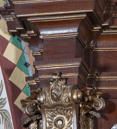 Zdjęcie nr 14: Ołtarz architektoniczny, jednoosiowy, z wydzieloną predellą, jednokondygnacyjny, ze zwieńczeniem. Mensa drewniana na skrzyniowej prostopadłościennej tumbie. Antependium w prostokątnej profilowanej ramie zdobione trzema płycinami, w których pośrodku płaskorzeźbione przedstawienie Chrystusa upadającego pod krzyżem, po bokach motywy serca. Nastawa ujęta kwadratowymi w rzucie filarami przyściennymi o kanelowanych trzonach, z kompozytowymi kapitelami, dźwigającymi występującymi nad nimi uproszczone belkowanie i profilowany gzyms, przerwany nad polem środkowym. Na tle filarów ustawione na konsolach rzeźby: Matka Boska Bolesna po lewej i św. Jan Ewangelista po prawej stronie. W polu środkowym barokowy obraz z przedstawieniem Ukrzyżowania w ozdobnej ramie. W przyłuczach ramy uskrzydlone główki aniołków. Poniżej obrazu nałożony motyw kielicha, po bokach dwie banderole z inskrypcją: BŁOGOSŁAWIONY KTÓRY / IDZIE W IMIĘ PAŃSKIE. Zwieńczenie w kształcie aedikuli o wklęsłych bokach, zamkniętej łukiem półkolistym nadwieszonym. W polu zwieńczenia obraz ukazujący św. Rozalię. Na gzymsie koronującym rzeźbione przedstawienie Boga Ojca oraz Gołębica Ducha Świętego. Poniżej obrazu medalion ze złoconymi literami: IHS. W osiach podpór dwa uskrzydlone anioły trzymające Arma Christi (trzcinę z gąbką i włócznię). Nastawa flankowana ażurowymi, płasko rzeźbionymi uszami w formie wici winnej latorośli z kiściami gron i liśćmi.  Struktura malowana na kolor brązowy, rzeźby, detale architektoniczne i ornamenty złocone lub srebrzone, część laserowana.