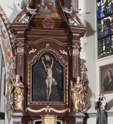 Zdjęcie nr 3: Prostopadłościenna szafka na rzucie prostokąta o ściętych od przodu narożnikach i od przodu opięta wysmukłymi kolumienkami o gładkich trzonach i kielichowych kapitelach, ustawionych na cokole i podtrzymujących profilowany gzyms w zwieńczeniu. W przedniej ściance prostokątne zamknięte półkoliście drzwiczki, osadzone na zawiasach i zamykane na zamek, wypełnione płaskorzeźbionymi literami A i Ω na tle promieni. Całe tabernakulum pozłocone.