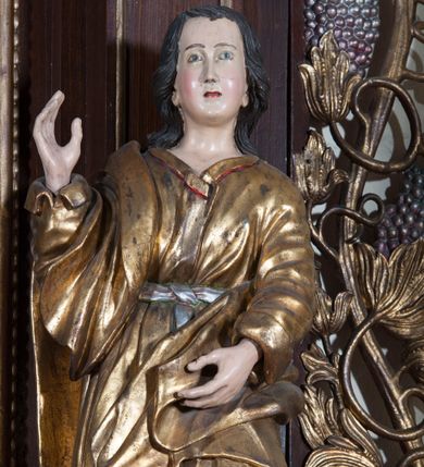Zdjęcie nr 1: Rzeźba pełnoplastyczna, przyścienna; przedstawienie św. Jana Ewangelisty ukazanego w całej postaci, stojącego w lekkim kontrapoście, z prawą nogą ugiętą w kolanie, zwróconego lekko w prawo i zapatrzonego przed siebie. Ręce ugięte w łokciach, prawa z dłonią wzniesioną ku górze, lewa z dłonią na wysokości brzucha. Twarz młodzieńcza, o jasnej karnacji i delikatnych rysach, z wysokim czołem, bez zarostu, okolona włosami sięgającymi po bokach do uszu, a z tyłu spływającymi na plecy. Ubrana w długą luźną, przepasaną w talii suknię z długimi szerokimi rękawami, osłania przód postaci.