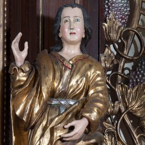 Zdjęcie nr 1: Rzeźba pełnoplastyczna, przyścienna; przedstawienie św. Jana Ewangelisty ukazanego w całej postaci, stojącego w lekkim kontrapoście, z prawą nogą ugiętą w kolanie, zwróconego lekko w prawo i zapatrzonego przed siebie. Ręce ugięte w łokciach, prawa z dłonią wzniesioną ku górze, lewa z dłonią na wysokości brzucha. Twarz młodzieńcza, o jasnej karnacji i delikatnych rysach, z wysokim czołem, bez zarostu, okolona włosami sięgającymi po bokach do uszu, a z tyłu spływającymi na plecy. Ubrana w długą luźną, przepasaną w talii suknię z długimi szerokimi rękawami, osłania przód postaci.