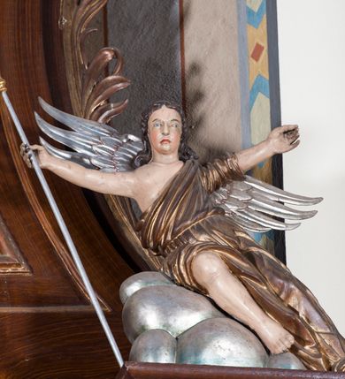 Zdjęcie nr 2: Dwie pełnoplastyczne przyścienne rzeźby, przedstawiające w całej postaci dwa siedzące w antytetycznych pozach uskrzydlone anioły. W rozłożonych na boki rękach trzymają: trzcinę z gąbką (anioł po lewej) i dzidę (anioł po prawej). Anioły, okryte złotą draperią, siedzą ukośnie na srebrzystych obłokach.  