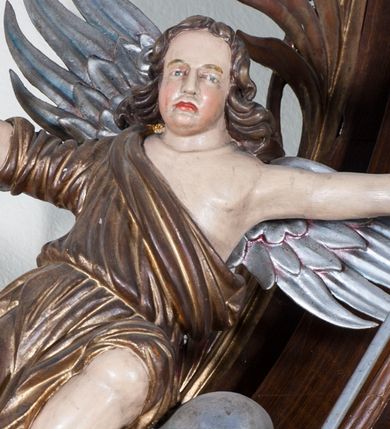 Zdjęcie nr 1: Dwie pełnoplastyczne przyścienne rzeźby, przedstawiające w całej postaci dwa siedzące w antytetycznych pozach uskrzydlone anioły. W rozłożonych na boki rękach trzymają: trzcinę z gąbką (anioł po lewej) i dzidę (anioł po prawej). Anioły, okryte złotą draperią, siedzą ukośnie na srebrzystych obłokach.  