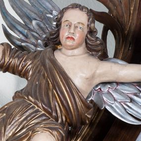 Zdjęcie nr 1: Dwie pełnoplastyczne przyścienne rzeźby, przedstawiające w całej postaci dwa siedzące w antytetycznych pozach uskrzydlone anioły. W rozłożonych na boki rękach trzymają: trzcinę z gąbką (anioł po lewej) i dzidę (anioł po prawej). Anioły, okryte złotą draperią, siedzą ukośnie na srebrzystych obłokach.  
