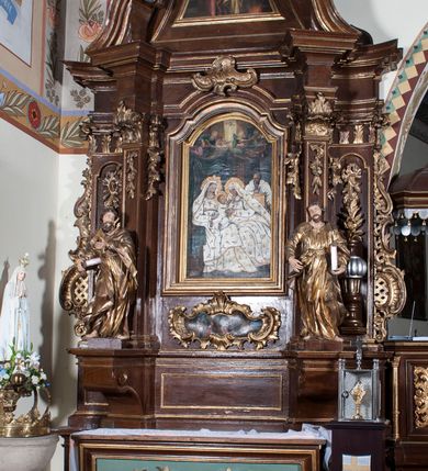 Zdjęcie nr 6: Ołtarz architektoniczny, jednokondygnacyjny, jednoosiowy ze zwieńczeniem. Antepedium z płaskorzeźbionym krzyżem ujętym wolutami z motywami lilii. Nastawę ujmują ukośnie ustawione zwielokrotnione  pilastry z konsolami, na których stoją figury. Pilastry podtrzymują belkowanie, które nad zewnętrznymi pilastrami jest lekko wklęsłe, nad wewnętrznymi zwieńczone falującymi naczółkami, a nad osią środkową  z lekko wybrzuszonym architrawem. Zwieńczenie o lekko wklęsłych bokach zamknięte profilowanym gzymsem w formie łuku nadwieszonego. W polu środkowym wnęka w kształcie stojącego prostokąta zakończonego łukiem odcinkowym, nadwieszonym, w niej obraz &quot;Św. Anna Samotrzeć&quot; i &quot;Męczeństwo św. Sebastiana&quot; na zasuwie. Pole obrazowe w zwieńczeniu powtarza jego kształt, wypełnione wizerunkiem św. Floriana. W partii predelli wkomponowano fantazyjny kartusz z obrazem przedstawiającym hołd Trzech Króli. Na dekorację ornamentalną składają się motywy rocaille&#039;owe na pilastrach, uszy ujmujące nastawę z rocaille&#039;ami w części wypełnionymi kratką regencyjną, kartusz w partii belkowania oraz drobne motywy roślinne i rokokowe w partii zwieńczenia., 

