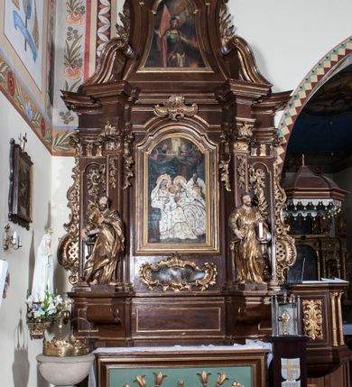 Zdjęcie nr 5: Ołtarz architektoniczny, jednokondygnacyjny, jednoosiowy ze zwieńczeniem. Antepedium z płaskorzeźbionym krzyżem ujętym wolutami z motywami lilii. Nastawę ujmują ukośnie ustawione zwielokrotnione  pilastry z konsolami, na których stoją figury. Pilastry podtrzymują belkowanie, które nad zewnętrznymi pilastrami jest lekko wklęsłe, nad wewnętrznymi zwieńczone falującymi naczółkami, a nad osią środkową  z lekko wybrzuszonym architrawem. Zwieńczenie o lekko wklęsłych bokach zamknięte profilowanym gzymsem w formie łuku nadwieszonego. W polu środkowym wnęka w kształcie stojącego prostokąta zakończonego łukiem odcinkowym, nadwieszonym, w niej obraz "Św. Anna Samotrzeć" i "Męczeństwo św. Sebastiana" na zasuwie. Pole obrazowe w zwieńczeniu powtarza jego kształt, wypełnione wizerunkiem św. Floriana. W partii predelli wkomponowano fantazyjny kartusz z obrazem przedstawiającym hołd Trzech Króli. Na dekorację ornamentalną składają się motywy rocaille'owe na pilastrach, uszy ujmujące nastawę z rocaille'ami w części wypełnionymi kratką regencyjną, kartusz w partii belkowania oraz drobne motywy roślinne i rokokowe w partii zwieńczenia., 

