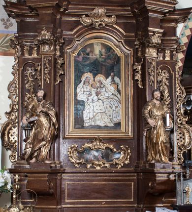 Zdjęcie nr 1: Ołtarz architektoniczny, jednokondygnacyjny, jednoosiowy ze zwieńczeniem. Antepedium z płaskorzeźbionym krzyżem ujętym wolutami z motywami lilii. Nastawę ujmują ukośnie ustawione zwielokrotnione  pilastry z konsolami, na których stoją figury. Pilastry podtrzymują belkowanie, które nad zewnętrznymi pilastrami jest lekko wklęsłe, nad wewnętrznymi zwieńczone falującymi naczółkami, a nad osią środkową  z lekko wybrzuszonym architrawem. Zwieńczenie o lekko wklęsłych bokach zamknięte profilowanym gzymsem w formie łuku nadwieszonego. W polu środkowym wnęka w kształcie stojącego prostokąta zakończonego łukiem odcinkowym, nadwieszonym, w niej obraz "Św. Anna Samotrzeć" i "Męczeństwo św. Sebastiana" na zasuwie. Pole obrazowe w zwieńczeniu powtarza jego kształt, wypełnione wizerunkiem św. Floriana. W partii predelli wkomponowano fantazyjny kartusz z obrazem przedstawiającym hołd Trzech Króli. Na dekorację ornamentalną składają się motywy rocaille'owe na pilastrach, uszy ujmujące nastawę z rocaille'ami w części wypełnionymi kratką regencyjną, kartusz w partii belkowania oraz drobne motywy roślinne i rokokowe w partii zwieńczenia., 

