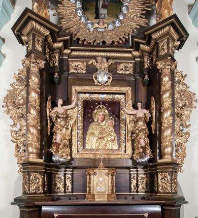 Zdjęcie nr 1: Ołtarz architektoniczny, jednoosiowy, z wydzieloną predellą, jednokondygnacyjny, ze zwieńczeniem. Mensa na prostopadłościennej, skrzyniowej tumbie z antependium ozdobionym prostokątną płyciną ze złoconym medalionem z ulistnioną gałązką pośrodku. Nastawa ujęta ustawionymi ukośnie kolumnami o skręconych trzonach oplecionych girlandą z liści i owoców, na cokołach, z kompozytowymi kapitelami, ustawionymi na dwustrefowych prostopadłościennych postumentach. Kolumny wspierają występujące nad nimi uproszczone belkowanie i profilowany gzyms, cofnięte nad polem środkowym. W polu nastawy prostokątna nisza ujęta ozdobną ramą, w której obraz Matki Boskiej z Dzieciątkiem oraz na zasuwie obraz Matki Boskiej Różańcowej ze św. Dominikiem i św. Katarzyną ze Sieny. Po bokach obrazu rzeźby dwóch uskrzydlonych aniołów, umieszczone na konsolach. Ponad obrazem pośrodku dwie główki aniołków ze skrzydełkami oraz kolisty wypukły medalion ze splecionymi literami imienia Maria; po bokach wolutowo zwinięte liście akantu. W zwieńczeniu duży obraz z przedstawieniem św. Jacka, w kształcie tonda, ujęty srebrnymi obłokami i główkami aniołków oraz glorią promienistą. W osiach podpór rzeźby dwóch nieokreślonych świętych w mitrach książęcych na głowach. Retabulum flankowane płaskorzeźbionymi, ażurowymi uszami, zbudowanymi z motywów karbowanej wstęgi i liści akantu. Struktura malowana w kolorze brązowym, rzeźby, detale architektoniczne i ornamenty złocone, niektóre srebrzone. 