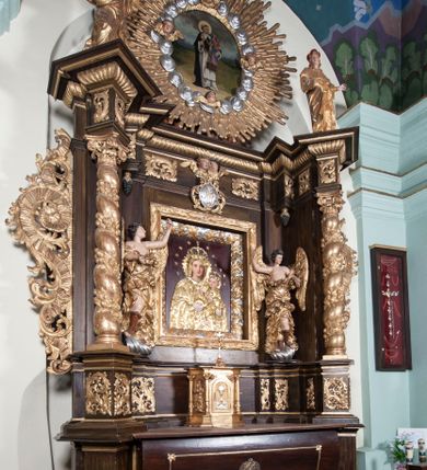 Zdjęcie nr 2: Ołtarz architektoniczny, jednoosiowy, z wydzieloną predellą, jednokondygnacyjny, ze zwieńczeniem. Mensa na prostopadłościennej, skrzyniowej tumbie z antependium ozdobionym prostokątną płyciną ze złoconym medalionem z ulistnioną gałązką pośrodku. Nastawa ujęta ustawionymi ukośnie kolumnami o skręconych trzonach oplecionych girlandą z liści i owoców, na cokołach, z kompozytowymi kapitelami, ustawionymi na dwustrefowych prostopadłościennych postumentach. Kolumny wspierają występujące nad nimi uproszczone belkowanie i profilowany gzyms, cofnięte nad polem środkowym. W polu nastawy prostokątna nisza ujęta ozdobną ramą, w której obraz Matki Boskiej z Dzieciątkiem oraz na zasuwie obraz Matki Boskiej Różańcowej ze św. Dominikiem i św. Katarzyną ze Sieny. Po bokach obrazu rzeźby dwóch uskrzydlonych aniołów, umieszczone na konsolach. Ponad obrazem pośrodku dwie główki aniołków ze skrzydełkami oraz kolisty wypukły medalion ze splecionymi literami imienia Maria; po bokach wolutowo zwinięte liście akantu. W zwieńczeniu duży obraz z przedstawieniem św. Jacka, w kształcie tonda, ujęty srebrnymi obłokami i główkami aniołków oraz glorią promienistą. W osiach podpór rzeźby dwóch nieokreślonych świętych w mitrach książęcych na głowach. Retabulum flankowane płaskorzeźbionymi, ażurowymi uszami, zbudowanymi z motywów karbowanej wstęgi i liści akantu. Struktura malowana w kolorze brązowym, rzeźby, detale architektoniczne i ornamenty złocone, niektóre srebrzone. 