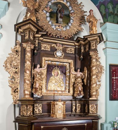 Zdjęcie nr 13: Ołtarz architektoniczny, jednoosiowy, z wydzieloną predellą, jednokondygnacyjny, ze zwieńczeniem. Mensa na prostopadłościennej, skrzyniowej tumbie z antependium ozdobionym prostokątną płyciną ze złoconym medalionem z ulistnioną gałązką pośrodku. Nastawa ujęta ustawionymi ukośnie kolumnami o skręconych trzonach oplecionych girlandą z liści i owoców, na cokołach, z kompozytowymi kapitelami, ustawionymi na dwustrefowych prostopadłościennych postumentach. Kolumny wspierają występujące nad nimi uproszczone belkowanie i profilowany gzyms, cofnięte nad polem środkowym. W polu nastawy prostokątna nisza ujęta ozdobną ramą, w której obraz Matki Boskiej z Dzieciątkiem oraz na zasuwie obraz Matki Boskiej Różańcowej ze św. Dominikiem i św. Katarzyną ze Sieny. Po bokach obrazu rzeźby dwóch uskrzydlonych aniołów, umieszczone na konsolach. Ponad obrazem pośrodku dwie główki aniołków ze skrzydełkami oraz kolisty wypukły medalion ze splecionymi literami imienia Maria; po bokach wolutowo zwinięte liście akantu. W zwieńczeniu duży obraz z przedstawieniem św. Jacka, w kształcie tonda, ujęty srebrnymi obłokami i główkami aniołków oraz glorią promienistą. W osiach podpór rzeźby dwóch nieokreślonych świętych w mitrach książęcych na głowach. Retabulum flankowane płaskorzeźbionymi, ażurowymi uszami, zbudowanymi z motywów karbowanej wstęgi i liści akantu. Struktura malowana w kolorze brązowym, rzeźby, detale architektoniczne i ornamenty złocone, niektóre srebrzone. 