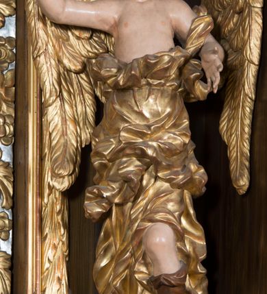 Zdjęcie nr 3: Rzeźby pełnoplastyczne, przyścienne wyobrażające dwóch aniołów ze skrzydłami, ukazanych w całej postaci, w antytetycznych pozach, w kontrapoście, w trzech czwartych zwróconych ku środkowi ołtarza, z głowami skierowanymi do widza. Anioł po prawej prawą ręką uniesioną na wysokość barku, a anioł po lewej lewą ręką wskazują wymownym gestem na obraz Matki Boskiej umieszczony w retabulum. Obaj aniołowie o młodzieńczych twarzach okolonych ciemnymi kędzierzawymi włosami. Ramiona i tors nagie, o jasnej karnacji. Brzuch, biodra i uda okryte silnie pofałdowaną dynamicznie złotą draperią spływającą z tyłu postaci aż do ziemi. Na nogach wysokie buty odsłaniające palce.  Pod stopami srebrzyste laserowane na niebiesko obłoki.