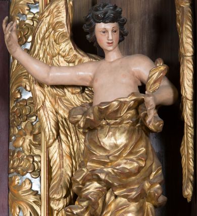Zdjęcie nr 1: Rzeźby pełnoplastyczne, przyścienne wyobrażające dwóch aniołów ze skrzydłami, ukazanych w całej postaci, w antytetycznych pozach, w kontrapoście, w trzech czwartych zwróconych ku środkowi ołtarza, z głowami skierowanymi do widza. Anioł po prawej prawą ręką uniesioną na wysokość barku, a anioł po lewej lewą ręką wskazują wymownym gestem na obraz Matki Boskiej umieszczony w retabulum. Obaj aniołowie o młodzieńczych twarzach okolonych ciemnymi kędzierzawymi włosami. Ramiona i tors nagie, o jasnej karnacji. Brzuch, biodra i uda okryte silnie pofałdowaną dynamicznie złotą draperią spływającą z tyłu postaci aż do ziemi. Na nogach wysokie buty odsłaniające palce.  Pod stopami srebrzyste laserowane na niebiesko obłoki.
