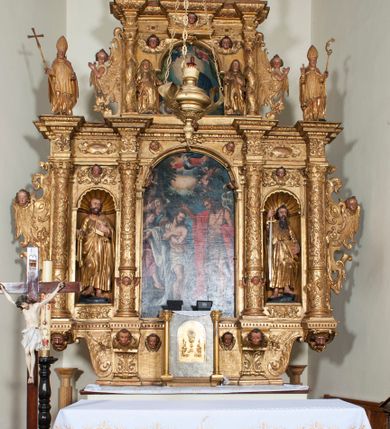 Zdjęcie nr 13: Ołtarz architektoniczny, z wydzieloną predellą, trójosiowy, dwukondygnacyjny ze zwieńczeniem. Predella węższa od nastawy, rozszerzająca się ku górze. Dolna kondygnacja artykułowana kolumnami o trzonach przedzielonych opaską w jednej trzeciej wysokości, zdobionych główkami aniołków, girlandami i dekoracją kandelabrową; kapitele kompozytowe; w osiach zewnętrznych kolumny nadwieszone na konsolach, w osiach wewnętrznych ustawione na postumentach. Kolumny wspierają belkowanie i gzyms występujące nad nimi. W polu środkowym prostokątna nisza zamknięta półkoliście, w niej obraz: Chrzest Chrystusa; w polach bocznych mniejsze nisze prostokątne zamknięte półkoliście, muszlowe, w nich rzeźby: Św. Piotr i Św. Paweł. Górna kondygnacja ujęta kolumnami o kręconych trzonach z dekoracją roślinną i kompozytowych kapitelach, wspierającymi belkowanie i profilowany gzyms. W polu środkowym nisza zamknięta półkoliście w niej obraz: Matka Boska z Dzieciątkiem. Po bokach obrazu rzeźby: Św. Anna (?) i Św. Marcin (?). Dolna i górna kondygnacje flankowane rzeźbionymi, ażurowymi uszakami z motywem herm aniołów. W osiach kolumn dolnej kondygnacji rzeźby: Św. Wojciech i Św. Stanisław. Zwieńczenie w kształcie półkolistego przyczółka wspartego na konsoli wchodzącej w pole górnej kondygnacji. W polu zwieńczenia płaskorzeźbione, półplastyczne przedstawienie Boga Ojca w popiersiu, flankowane wolutami z półpostaciami dwóch uskrzydlonych aniołów. Po bokach w zwieńczeniu, w osiach kolumn górnej kondygnacji, rzeźby uskrzydlonych aniołów.   W szczycie ołtarza na konsoli rzeźba: Św. Michał Archanioł. W przyłuczach nisz na obrazy, ponad niszami na rzeźby, w predelli, na konsolach i postumentach kolumn dolnej kondygnacji oraz na konsoli poniżej zwieńczenia uskrzydlone główki aniołków. Ponadto poniżej nisz, w tle kolumn oraz na belkowaniu płyciny ornamentalne z motywów roślinnych i motywy rautów. Struktura ołtarza, rzeźby i ornamenty złocone, karnacje i włosy polichromowane.  
