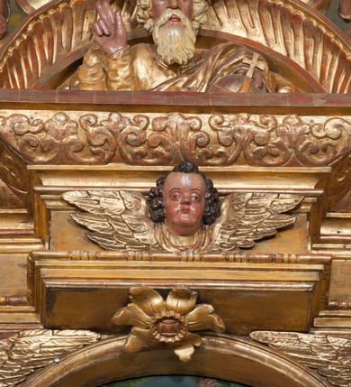 Zdjęcie nr 54: Ołtarz architektoniczny, z wydzieloną predellą, trójosiowy, dwukondygnacyjny ze zwieńczeniem. Predella węższa od nastawy, rozszerzająca się ku górze. Dolna kondygnacja artykułowana kolumnami o trzonach przedzielonych opaską w jednej trzeciej wysokości, zdobionych główkami aniołków, girlandami i dekoracją kandelabrową; kapitele kompozytowe; w osiach zewnętrznych kolumny nadwieszone na konsolach, w osiach wewnętrznych ustawione na postumentach. Kolumny wspierają belkowanie i gzyms występujące nad nimi. W polu środkowym prostokątna nisza zamknięta półkoliście, w niej obraz: Chrzest Chrystusa; w polach bocznych mniejsze nisze prostokątne zamknięte półkoliście, muszlowe, w nich rzeźby: Św. Piotr i Św. Paweł. Górna kondygnacja ujęta kolumnami o kręconych trzonach z dekoracją roślinną i kompozytowych kapitelach, wspierającymi belkowanie i profilowany gzyms. W polu środkowym nisza zamknięta półkoliście w niej obraz: Matka Boska z Dzieciątkiem. Po bokach obrazu rzeźby: Św. Anna (?) i Św. Marcin (?). Dolna i górna kondygnacje flankowane rzeźbionymi, ażurowymi uszakami z motywem herm aniołów. W osiach kolumn dolnej kondygnacji rzeźby: Św. Wojciech i Św. Stanisław. Zwieńczenie w kształcie półkolistego przyczółka wspartego na konsoli wchodzącej w pole górnej kondygnacji. W polu zwieńczenia płaskorzeźbione, półplastyczne przedstawienie Boga Ojca w popiersiu, flankowane wolutami z półpostaciami dwóch uskrzydlonych aniołów. Po bokach w zwieńczeniu, w osiach kolumn górnej kondygnacji, rzeźby uskrzydlonych aniołów.   W szczycie ołtarza na konsoli rzeźba: Św. Michał Archanioł. W przyłuczach nisz na obrazy, ponad niszami na rzeźby, w predelli, na konsolach i postumentach kolumn dolnej kondygnacji oraz na konsoli poniżej zwieńczenia uskrzydlone główki aniołków. Ponadto poniżej nisz, w tle kolumn oraz na belkowaniu płyciny ornamentalne z motywów roślinnych i motywy rautów. Struktura ołtarza, rzeźby i ornamenty złocone, karnacje i włosy polichromowane.  
