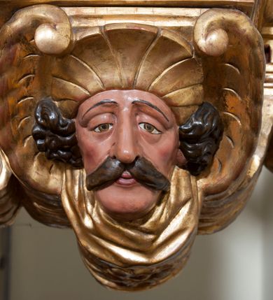 Zdjęcie nr 34: Ołtarz architektoniczny, z wydzieloną predellą, trójosiowy, dwukondygnacyjny ze zwieńczeniem. Predella węższa od nastawy, rozszerzająca się ku górze. Dolna kondygnacja artykułowana kolumnami o trzonach przedzielonych opaską w jednej trzeciej wysokości, zdobionych główkami aniołków, girlandami i dekoracją kandelabrową; kapitele kompozytowe; w osiach zewnętrznych kolumny nadwieszone na konsolach, w osiach wewnętrznych ustawione na postumentach. Kolumny wspierają belkowanie i gzyms występujące nad nimi. W polu środkowym prostokątna nisza zamknięta półkoliście, w niej obraz: Chrzest Chrystusa; w polach bocznych mniejsze nisze prostokątne zamknięte półkoliście, muszlowe, w nich rzeźby: Św. Piotr i Św. Paweł. Górna kondygnacja ujęta kolumnami o kręconych trzonach z dekoracją roślinną i kompozytowych kapitelach, wspierającymi belkowanie i profilowany gzyms. W polu środkowym nisza zamknięta półkoliście w niej obraz: Matka Boska z Dzieciątkiem. Po bokach obrazu rzeźby: Św. Anna (?) i Św. Marcin (?). Dolna i górna kondygnacje flankowane rzeźbionymi, ażurowymi uszakami z motywem herm aniołów. W osiach kolumn dolnej kondygnacji rzeźby: Św. Wojciech i Św. Stanisław. Zwieńczenie w kształcie półkolistego przyczółka wspartego na konsoli wchodzącej w pole górnej kondygnacji. W polu zwieńczenia płaskorzeźbione, półplastyczne przedstawienie Boga Ojca w popiersiu, flankowane wolutami z półpostaciami dwóch uskrzydlonych aniołów. Po bokach w zwieńczeniu, w osiach kolumn górnej kondygnacji, rzeźby uskrzydlonych aniołów.   W szczycie ołtarza na konsoli rzeźba: Św. Michał Archanioł. W przyłuczach nisz na obrazy, ponad niszami na rzeźby, w predelli, na konsolach i postumentach kolumn dolnej kondygnacji oraz na konsoli poniżej zwieńczenia uskrzydlone główki aniołków. Ponadto poniżej nisz, w tle kolumn oraz na belkowaniu płyciny ornamentalne z motywów roślinnych i motywy rautów. Struktura ołtarza, rzeźby i ornamenty złocone, karnacje i włosy polichromowane.  
