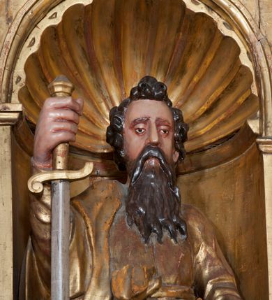 Zdjęcie nr 4: Rzeźba pełnoplastyczna, przyścienna, ścięta z tyłu. Figura zwrócona frontalnie do widza, święty lewą nogę opiera na rzeźbionym fragmencie skały; w prawej ręce unosi zwrócony ostrzem w dół duży miecz, lewą podtrzymuje opartą na biodrze księgę. Twarz pociągła, o głęboko osadzonych, półprzymkniętych oczach, dużym prostym nosie, okolona długą brodą opadającą na pierś. Włosy krótkie, falowane. Święty ubrany w tunikę z długimi rękawami, przepasaną w talii, u dołu obficie drapowaną w równoległe fałdy oraz płaszcz przerzucony przez prawe ramię i przewieszony przez pas na lewym boku. Figura delikatnie poruszona, o niewłaściwych proporcjach anatomicznych. Polichromia naturalistyczna w partiach ciała, szaty złocone, miecz srebrzony.