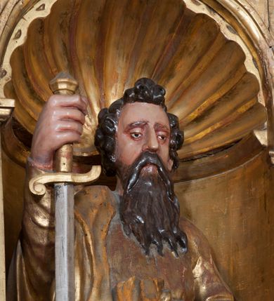 Zdjęcie nr 6: Rzeźba pełnoplastyczna, przyścienna, ścięta z tyłu. Figura zwrócona frontalnie do widza, święty lewą nogę opiera na rzeźbionym fragmencie skały; w prawej ręce unosi zwrócony ostrzem w dół duży miecz, lewą podtrzymuje opartą na biodrze księgę. Twarz pociągła, o głęboko osadzonych, półprzymkniętych oczach, dużym prostym nosie, okolona długą brodą opadającą na pierś. Włosy krótkie, falowane. Święty ubrany w tunikę z długimi rękawami, przepasaną w talii, u dołu obficie drapowaną w równoległe fałdy oraz płaszcz przerzucony przez prawe ramię i przewieszony przez pas na lewym boku. Figura delikatnie poruszona, o niewłaściwych proporcjach anatomicznych. Polichromia naturalistyczna w partiach ciała, szaty złocone, miecz srebrzony.