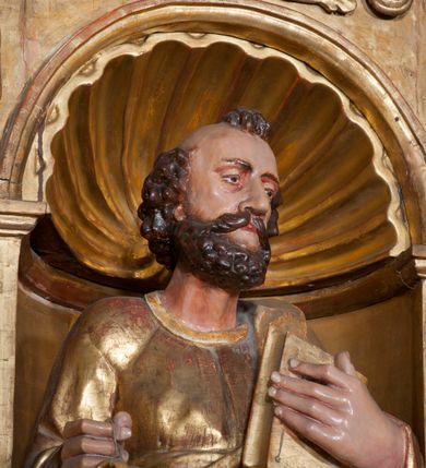 Zdjęcie nr 5: Rzeźba pełnoplastyczna, przyścienna, ścięta z tyłu. Figura zwrócona frontalnie do widza, z głową skierowaną w prawą stronę. Święty prawą nogę opiera na rzeźbionym fragmencie skały; w prawej, wyciągniętej przed siebie ręce trzyma klucze, lewą podtrzymuje przy piersi księgę. Twarz pociągła, o głęboko osadzonych, półprzymkniętych oczach, dużym prostym nosie, okolona brodą. Włosy krótkie, falowane w postaci pukli po bokach i na czubku głowy. Święty ubrany w tunikę z długimi rękawami, przepasaną w talii, u dołu obficie drapowaną w równoległe fałdy, oraz płaszcz przerzucony przez lewe ramię oraz przewieszony przez pas na prawym boku. Rzeźba, delikatnie poruszona, o zaburzonych proporcjach ciała. Polichromia naturalistyczna w partiach ciała, szaty złocone.