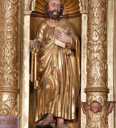 Zdjęcie nr 2: Rzeźba pełnoplastyczna, przyścienna, ścięta z tyłu. Figura zwrócona frontalnie do widza, z głową skierowaną w prawą stronę. Święty prawą nogę opiera na rzeźbionym fragmencie skały; w prawej, wyciągniętej przed siebie ręce trzyma klucze, lewą podtrzymuje przy piersi księgę. Twarz pociągła, o głęboko osadzonych, półprzymkniętych oczach, dużym prostym nosie, okolona brodą. Włosy krótkie, falowane w postaci pukli po bokach i na czubku głowy. Święty ubrany w tunikę z długimi rękawami, przepasaną w talii, u dołu obficie drapowaną w równoległe fałdy, oraz płaszcz przerzucony przez lewe ramię oraz przewieszony przez pas na prawym boku. Rzeźba, delikatnie poruszona, o zaburzonych proporcjach ciała. Polichromia naturalistyczna w partiach ciała, szaty złocone.