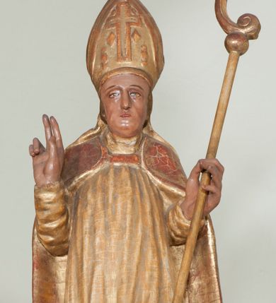 Zdjęcie nr 1: Rzeźba pełnoplastyczna, przyścienna, ścięta z tyłu. Święty, ukazany frontalnie, stoi z rękami ugiętymi w łokciach, prawą błogosławi, lewą podtrzymuje pastorał. Twarz kwadratowa, o wyraźnej linii żuchwy, małych oczach, prostym nosie i niewielkich ustach. Święty ubrany w długą albę, komżę, spiętą pod szyją kapę, na głowie infułą ozdobiona dużym krzyżem. Polichromia naturalistyczna w partiach ciała, szaty złocone.