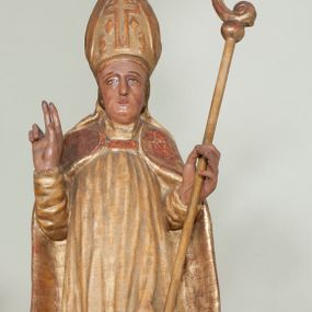 Zdjęcie nr 1: Rzeźba pełnoplastyczna, przyścienna, ścięta z tyłu. Święty, ukazany frontalnie, stoi z rękami ugiętymi w łokciach, prawą błogosławi, lewą podtrzymuje pastorał. Twarz kwadratowa, o wyraźnej linii żuchwy, małych oczach, prostym nosie i niewielkich ustach. Święty ubrany w długą albę, komżę, spiętą pod szyją kapę, na głowie infułą ozdobiona dużym krzyżem. Polichromia naturalistyczna w partiach ciała, szaty złocone.
