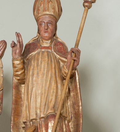 Zdjęcie nr 2: Rzeźba pełnoplastyczna, przyścienna, ścięta z tyłu. Święty, ukazany frontalnie, stoi z rękami ugiętymi w łokciach, prawą błogosławi, lewą podtrzymuje pastorał. Twarz kwadratowa, o wyraźnej linii żuchwy, małych oczach, prostym nosie i niewielkich ustach. Święty ubrany w długą albę, komżę, spiętą pod szyją kapę, na głowie infułą ozdobiona dużym krzyżem. Polichromia naturalistyczna w partiach ciała, szaty złocone.