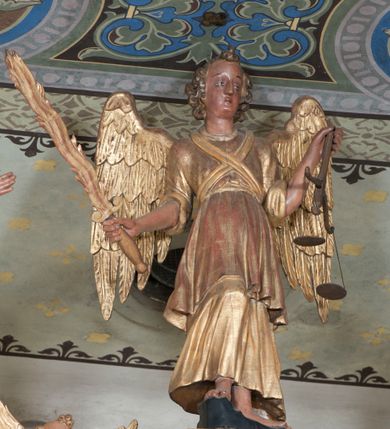 Zdjęcie nr 2: Rzeźba pełnoplastyczna, przyścienna, ścięta z tyłu. Archanioł, ukazany frontalnie, stoi w lekkim kontrapoście, prawą nogę opierając na rzeźbionym fragmencie skały. W prawej ręce unosi zwrócony ostrzem do góry płonący miecz, w lewej trzyma wagę. Twarz szczupła, o młodzieńczych rysach. Włosy krótkie, układające się gęstymi puklami, z czubem pośrodku. Ubrany w długą szatę spodnią, szatę wierzchnią sięgającą do kolan i przepasaną w talii, na piersiach skrzyżowana szarfa. Skrzydła rozłożone na boki. Polichromia naturalistyczna w partiach ciała, szaty i atrybuty złocone.