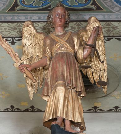 Zdjęcie nr 1: Rzeźba pełnoplastyczna, przyścienna, ścięta z tyłu. Archanioł, ukazany frontalnie, stoi w lekkim kontrapoście, prawą nogę opierając na rzeźbionym fragmencie skały. W prawej ręce unosi zwrócony ostrzem do góry płonący miecz, w lewej trzyma wagę. Twarz szczupła, o młodzieńczych rysach. Włosy krótkie, układające się gęstymi puklami, z czubem pośrodku. Ubrany w długą szatę spodnią, szatę wierzchnią sięgającą do kolan i przepasaną w talii, na piersiach skrzyżowana szarfa. Skrzydła rozłożone na boki. Polichromia naturalistyczna w partiach ciała, szaty i atrybuty złocone.