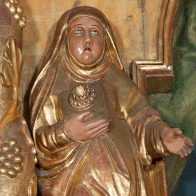 Zdjęcie nr 1: Rzeźba pełnoplastyczna, przyścienna, ścięta z tyłu. Święta ukazana frontalnie, w lekkim kontrapoście, z prawą nogą ugiętą w kolanie i wysuniętą stopą. Ręce ugięte w łokciach. Prawą dłonią przyciska przez połę płaszcza nierozpoznany przedmiot; lewą wyciąga przed siebie. Twarz okrągła, pełna, o rysach dojrzałej kobiety, oczy zwrócone ku górze. Ubrana w przewiązaną w pasie tunikę oraz płaszcz podwinięty pod prawą ręką i odsłaniający prawą nogę, na głowie długi welon z podwiką. Polichromia naturalistyczna w partiach ciała, szaty złocone.