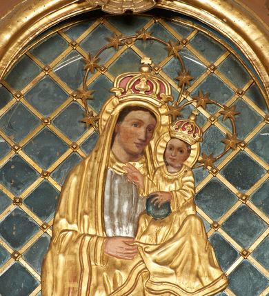 Zdjęcie nr 2: Obraz w formie stojącego prostokąta zamkniętego łukiem półkolistym nadwieszonym. Twarze postaci malowane są na płótnie, pozostałe elementy są płaskorzeźbione. W centrum kompozycji całopostaciowe przedstawienie Matki Boskiej z Dzieciątkiem stojącej na globie i sierpie księżyca. Maria ukazana jest frontalnie, z opuszczoną głową skierowaną w lewo, prawą, ugiętą rękę trzyma z przodu, lewą podtrzymuje Dzieciątko. Twarz ma owalną, o dużych, okrągłych oczach i nosie, pełnych ustach, okoloną brązowymi włosami. Ubrana jest w srebrzoną, długą suknię oraz długi, złocony płaszcz zarzucony na głowę i ramiona. Dzieciątko ukazane jest w pozycji siedzącej, zwrócone w trzech czwartych w prawo. Lewą ręką przytrzymuje na kolanie kulę, prawą unosi w geście błogosławieństwa. Twarz ma okrągłą, o dużych oczach, małym nosie i pełnych ustach, okoloną jasnobrązowymi, krótkimi włosami. Ubrane jest w luźną, złoconą tunikę. Na głowach obu postaci korony zamknięte, wokół nich nimby zamknięte i gwieździste. Maria i Dzieciątko ukazane na tle kratki wypełnionej taflami lustra. Obraz ujęty złoconą ramą. 

