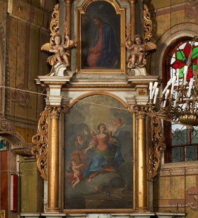 Zdjęcie nr 2: Obraz w formie stojącego prostokąta zamkniętego łukiem półkolistym nadwieszonym. W centrum kompozycji przedstawienie klęczącego Chrystusa zwróconego profilem w prawo, z opuszczoną głową oraz splecionymi dłońmi położonymi na kolanach. Twarz ma szczupłą, pociągłą, z dużym, prostym nosem, okrągłymi oczami skierowanymi w dół oraz pełnymi ustami, okoloną jasną, krótką brodą oraz jasnobrązowymi, falowanymi włosami opadającymi na plecy. Chrystus ubrany jest w jasnoczerwoną, długą tunikę oraz niebieski płaszcz narzucony na ramiona i plecy. Na stopach ma sandały. Przed postacią na obłoku unosi się uskrzydlona główka anielska z pateną i hostią na głowie. Za Chrystusem palma. Postać ukazana na tle pejzażu. Obraz ujęty profilowaną i złoconą ramą.