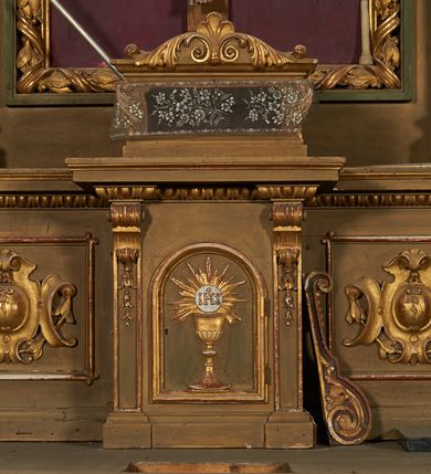 Zdjęcie nr 8: Nastawa ołtarzowa architektoniczna, jednoosiowa, jednokondygnacyjna ze zwieńczeniem. Ołtarz drewniany, prostopadłościenny, mensa drewniana. Nastawa ustawiona na cokole zakończonym gzymsem z motywem wolego oka, dekorowanym płycinami z kartuszami, z wyodrębnionym po środku tabernakulum flankowanym pilastrami z konsolami i kampanulami. Drzwiczki tabernakulum w formie stojącego prostokąta zamkniętego łukiem półkolistym z przedstawieniem kielicha z hostią w glorii. Nastawa ujęta parą zdwojonych filarów ustawionych pod kątem, o kanelowanych trzonach i kapitelach kompozytowych dźwigających fragmenty przerwanego belkowania dekorowanego wolim okiem oraz ćwierćkolistego, przerwanego przyczółka, na których siedzi para puttów. Na tle filarów, po zewnętrznej stronie ustawione są figury biskupów. W polu środkowym wnęka w formie stojącego prostokąta zamkniętego łukiem półkolistym nadwieszonym, ujęta grubą ramą dekorowaną wstęgą przeplataną z pąkami kwiatów, zwieńczona kartuszem; w polu figura Chrystusa Ukrzyżowanego na czerwonym tle. W przyłuczach dwie uskrzydlone główki anielskie. Zwieńczenie w formie stojącego prostokąta ujętego spływami wolutowymi, zamknięte fragmentem gzymsu, na którym znajduje się szczyt utworzony z przeciwstawnie zwróconych wolut z anthemionem. W polu zwieńczenia obraz w formie stojącego prostokąta z zaokrąglonymi górnymi narożami z przedstawieniem Matki Boskiej Bolesnej, ujęty profilowaną ramą. Ponad nim wić roślinna. Struktura ołtarza malowana na kolor jasnobrązowy, profile i ornamenty złocone.
