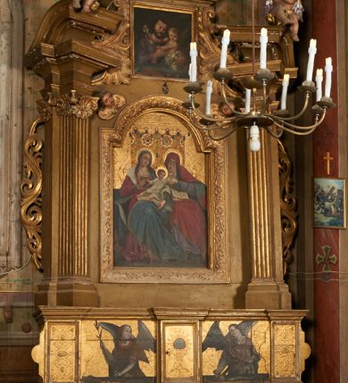 Zdjęcie nr 1: Nastawa ołtarzowa architektoniczna, jednoosiowa, jednokondygnacyjna ze zwieńczeniem. Ołtarz drewniany, prostopadłościenny, mensa drewniana. Antepedium w profilowanej ramie, z malowanym krzyżem, kotwicą i gorejącym sercem, w otoczeniu kwiatów. Predella na na niskim cokole, flankowana dwoma pilastrami, dźwigającymi gzyms wieńczący, wyłamany w partii pilastrów i tabernakulum po środku. Trzony pilastrów dekorowane ornamentem okuciowym z kaboszonami. W polach pomiędzy nimi malowane półpostacie aniołów, u spodu parapet z przedstawieniem arma Christi. Lewa postać z palmą, prawa ze włócznią i sakiewką. Ukazane na złoconym tle z tłoczonym ornamentem roślinnym. Drzwiczki tabernakulum w formie stojącego prostokąta z przedstawieniem kielicha z hostią z monogramen IHS, w glorii. Nastawa ujęta parą zdwojonych pilastrów zwróconych do wewnątrz, o kanelowanych trzonach i kapitelach kompozytowych dekorowanych rocaille'm. Podpory dźwigają fragmenty przerwanego belkowania i ćwierćkolistego, przerwanego przyczółka, na których siedzi para puttów. W polu środkowym płycina w formie stojącego prostokąta zamkniętego łukiem półkolistym nadwieszonym ujęta grubą ramą dekorowaną akantem z obrazem św. Anny Samotrzeć. W przyłuczach dwie uskrzydlone główki anielskie. Kondygnacja ujęta ażurowymi, akantowymi uszami. Zwieńczenie w formie stojącego prostokąta ujętego utworzonymi z rocaille'u i muszli spływami wolutowymi, zamknięte fragmentem gzymsu, na którym znajduje się szczyt utworzony z przeciwstawnie zwróconych wolut z anthemionem. W polu zwieńczenia obraz w formie stojącego prostokąta z przedstawieniem św. Józefa z Dzieciątkiem. Struktura ołtarza malowana na kolor jasnobrązowy, profile i ornamenty złocone.