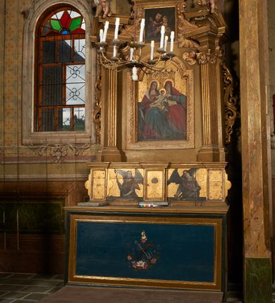 Zdjęcie nr 5: Nastawa ołtarzowa architektoniczna, jednoosiowa, jednokondygnacyjna ze zwieńczeniem. Ołtarz drewniany, prostopadłościenny, mensa drewniana. Antepedium w profilowanej ramie, z malowanym krzyżem, kotwicą i gorejącym sercem, w otoczeniu kwiatów. Predella na na niskim cokole, flankowana dwoma pilastrami, dźwigającymi gzyms wieńczący, wyłamany w partii pilastrów i tabernakulum po środku. Trzony pilastrów dekorowane ornamentem okuciowym z kaboszonami. W polach pomiędzy nimi malowane półpostacie aniołów, u spodu parapet z przedstawieniem arma Christi. Lewa postać z palmą, prawa ze włócznią i sakiewką. Ukazane na złoconym tle z tłoczonym ornamentem roślinnym. Drzwiczki tabernakulum w formie stojącego prostokąta z przedstawieniem kielicha z hostią z monogramen IHS, w glorii. Nastawa ujęta parą zdwojonych pilastrów zwróconych do wewnątrz, o kanelowanych trzonach i kapitelach kompozytowych dekorowanych rocaille'm. Podpory dźwigają fragmenty przerwanego belkowania i ćwierćkolistego, przerwanego przyczółka, na których siedzi para puttów. W polu środkowym płycina w formie stojącego prostokąta zamkniętego łukiem półkolistym nadwieszonym ujęta grubą ramą dekorowaną akantem z obrazem św. Anny Samotrzeć. W przyłuczach dwie uskrzydlone główki anielskie. Kondygnacja ujęta ażurowymi, akantowymi uszami. Zwieńczenie w formie stojącego prostokąta ujętego utworzonymi z rocaille'u i muszli spływami wolutowymi, zamknięte fragmentem gzymsu, na którym znajduje się szczyt utworzony z przeciwstawnie zwróconych wolut z anthemionem. W polu zwieńczenia obraz w formie stojącego prostokąta z przedstawieniem św. Józefa z Dzieciątkiem. Struktura ołtarza malowana na kolor jasnobrązowy, profile i ornamenty złocone.