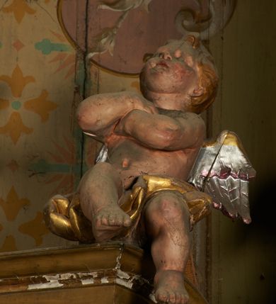 Zdjęcie nr 10: Nastawa ołtarzowa architektoniczna, jednoosiowa, jednokondygnacyjna ze zwieńczeniem. Ołtarz drewniany, prostopadłościenny, mensa drewniana. Antepedium w profilowanej ramie, z malowanym krzyżem, kotwicą i gorejącym sercem, w otoczeniu kwiatów. Predella na na niskim cokole, flankowana dwoma pilastrami, dźwigającymi gzyms wieńczący, wyłamany w partii pilastrów i tabernakulum po środku. Trzony pilastrów dekorowane ornamentem okuciowym z kaboszonami. W polach pomiędzy nimi malowane półpostacie aniołów, u spodu parapet z przedstawieniem arma Christi. Lewa postać z palmą, prawa ze włócznią i sakiewką. Ukazane na złoconym tle z tłoczonym ornamentem roślinnym. Drzwiczki tabernakulum w formie stojącego prostokąta z przedstawieniem kielicha z hostią z monogramen IHS, w glorii. Nastawa ujęta parą zdwojonych pilastrów zwróconych do wewnątrz, o kanelowanych trzonach i kapitelach kompozytowych dekorowanych rocaille'm. Podpory dźwigają fragmenty przerwanego belkowania i ćwierćkolistego, przerwanego przyczółka, na których siedzi para puttów. W polu środkowym płycina w formie stojącego prostokąta zamkniętego łukiem półkolistym nadwieszonym ujęta grubą ramą dekorowaną akantem z obrazem św. Anny Samotrzeć. W przyłuczach dwie uskrzydlone główki anielskie. Kondygnacja ujęta ażurowymi, akantowymi uszami. Zwieńczenie w formie stojącego prostokąta ujętego utworzonymi z rocaille'u i muszli spływami wolutowymi, zamknięte fragmentem gzymsu, na którym znajduje się szczyt utworzony z przeciwstawnie zwróconych wolut z anthemionem. W polu zwieńczenia obraz w formie stojącego prostokąta z przedstawieniem św. Józefa z Dzieciątkiem. Struktura ołtarza malowana na kolor jasnobrązowy, profile i ornamenty złocone.