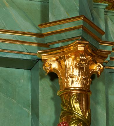 Zdjęcie nr 10: Nastawa architektoniczna, dwukondygnacyjna, jednoosiowa z bramkami. Ołtarz kamienny, w drewnianej prostopadłościennej obudowie, z drewnianą mensą. Na niej ustawione tabernakulum. Pierwsza kondygnacja na cokole z wyodrębnionymi dwoma prostopadłościanami, dekorowanym ornamentem roślinnym; ujęta parą kolumn o kapitelach kompozytowych oraz skręconych trzonach dekorowanych winną latoroślą. Podpory oraz konsole podtrzymują pełne belkowanie wyłamane pod kątem na ich osi, z architrawem przerwanym nad polem środkowym, oraz fragmenty falistego, przerwanego przyczółka, na którym znajdują się dwie siedzące figury aniołów. Fryz dekorowany rozetami, ornamentem roślinnym i kartuszem. W polu środkowym wnęka w formie stojącego prostokąta ujęta ramą dekorowaną płaskorzeźbionym wieńcem, w niej obraz Trójcy Świętej w osobnej ramie zdobionej ornamentem roślinnym. Druga kondygnacja na niskim cokole z wyodrębnionymi prostopadłościanami, flankowana parą pilastrów zakończonych konsolami podtrzymującymi belkowanie, wyłamane na ich osi. Całe pole wypełnia wnęka w formie  prostokąta zbliżonego do kwadratu ujęta ramą, wewnątrz obraz przedstawiający pokłon pasterzy w formie leżącego prostokąta o świętych narożach, w ramie dekorowanej ornamentem roślinnym, w narożach wnęki rozety. Na osi pilastrów, na belkowaniu muszle. Całość zakończona medalionem z gołębicą Ducha Świętego, otoczonego obłokami, w glorii promienistej. Obie kondygnacje ujęte uszami utworzonymi z ażurowego akantu. Bramki zamknięte trójbocznie z przejściami w formie stojącego prostokąta zamkniętego łukiem półkolistym nadwieszonym w ramie. Na bramkach ustawione figury św. Wojciecha i św. Stanisława. Struktura polichromowana w sposób imitujący jasnozielony marmur, profile, kolumny i ornamentyka złocone, obłoki srebrzone, winna latorośl laserowana. 