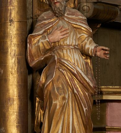 Zdjęcie nr 1: Figura drążona z tyłu, ustawiona na podstawie na nieregularnym planie. Święty ukazany frontalnie, z pochyloną głową skierowaną w prawo, prawa noga oparta na postumencie. Lewa ręka ugięta, wyciągnięta w bok, prawa złożona na piersi. Twarz ma podłużną, o wąskich, migdałowatych oczach, dużym nosie i wąskich, rozchylonych ustach, okoloną falowaną brodą oraz krótkimi włosami z grzywką nad czołem. Święty ubrany w złoconą, przylegającą do ciała, fałdowaną tunikę, przepasaną w talii oraz złocony płaszcz zapięty na piersi, opadający na ramiona z zarzuconą połą na prawą nogę. Polichromia ciała naturalistyczna.
