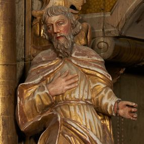 Zdjęcie nr 1: Figura drążona z tyłu, ustawiona na podstawie na nieregularnym planie. Święty ukazany frontalnie, z pochyloną głową skierowaną w prawo, prawa noga oparta na postumencie. Lewa ręka ugięta, wyciągnięta w bok, prawa złożona na piersi. Twarz ma podłużną, o wąskich, migdałowatych oczach, dużym nosie i wąskich, rozchylonych ustach, okoloną falowaną brodą oraz krótkimi włosami z grzywką nad czołem. Święty ubrany w złoconą, przylegającą do ciała, fałdowaną tunikę, przepasaną w talii oraz złocony płaszcz zapięty na piersi, opadający na ramiona z zarzuconą połą na prawą nogę. Polichromia ciała naturalistyczna.
