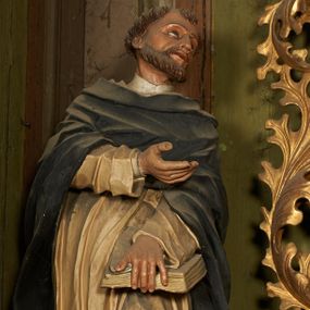 Zdjęcie nr 1: Figura drążona z tyłu, ustawiona na niewielkim postumencie. Święty ukazany frontalnie, pochylony w lewo, z uniesioną głową, w silnym kontrapoście. Lewą ręką przytrzymuje z przodu, na udzie księgę, prawą ugiętą, kieruje w lewo. Twarz ma szczupłą, o głęboko osadzonych, dużych oczach, skierowanych w górę, dużym nosie oraz wąskich, rozchylonych ustach. Twarz okolona jest krótką brodą oraz krótkimi włosami, na głowie tonsura. Święty ubrany w obficie fałdowany, biały habit dominikański oraz czarny płaszcz z kapturem. Polichromia ciała naturalistyczna.