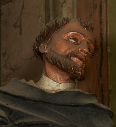 Zdjęcie nr 4: Figura drążona z tyłu, ustawiona na niewielkim postumencie. Święty ukazany frontalnie, pochylony w lewo, z uniesioną głową, w silnym kontrapoście. Lewą ręką przytrzymuje z przodu, na udzie księgę, prawą ugiętą, kieruje w lewo. Twarz ma szczupłą, o głęboko osadzonych, dużych oczach, skierowanych w górę, dużym nosie oraz wąskich, rozchylonych ustach. Twarz okolona jest krótką brodą oraz krótkimi włosami, na głowie tonsura. Święty ubrany w obficie fałdowany, biały habit dominikański oraz czarny płaszcz z kapturem. Polichromia ciała naturalistyczna.