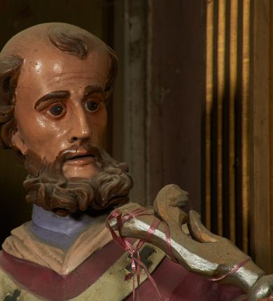 Zdjęcie nr 5: Figura drążona z tyłu, ustawiona na niewielkim prostopadłościennym postumencie. Święty ukazany jest frontalnie, lekko odchylony, z głową skierowaną w lewo, w kontrapoście. Obie ręce ma rozłożone na boki, w prawej dłoni trzyma kamień (?). Twarz ma szczupłą, wyciągniętą, o wysokim czole, silnie zaznaczonych kościach policzkowych; ma duże oczy, lekko garbaty nos oraz wąskie, rozchylone usta. Twarz okolona jest gęstą, brązową brodą, na głowie ma łysinę, po bokach głowy i nad czołem kręcone włosy. Święty ubrany jest w jasnofioletową sutannę, białą, złoconą przy brzegu komżę, czerwoną pelerynkę z różową podszewką oraz paliusz. Polichromia naturalistyczna w partiach ciała.