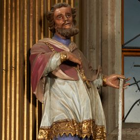 Zdjęcie nr 1: Figura drążona od tyłu, ustawiona na niewielkim prostopadłościennym postumencie. Święty ukazany jest frontalnie, w kontrapoście, o odchylonej sylwetce, z głową skierowaną w prawo. W lewej, ugiętej i odchylonej ręce trzyma laskę, prawą kładzie na piersi. Twarz ma szczupłą, podłużną o silnie zaznaczonych kościach policzkowych, dużych, migdałowatych oczach, lekko garbatym nosie i długich, wąskich, rozchylonych ustach, okoloną gęstą, brązową, kręconą brodą i kręconymi włosami. Święty ubrany jest w jasnofioletową sutannę, białą, złoconą przy brzegu komżę, czerwoną pelerynkę o różowej podszewce. Na piersi ma zawieszony pektorał. Przy lewej nodze biała, lamowana infuła ze złoconym krzyżem. Polichromia ciała naturalistyczna. 
