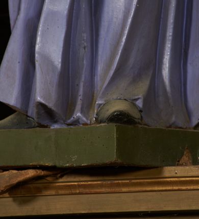 Zdjęcie nr 10: Figura drążona od tyłu, ustawiona na niewielkim prostopadłościennym postumencie. Święty ukazany jest frontalnie, w kontrapoście, o odchylonej sylwetce, z głową skierowaną w prawo. W lewej, ugiętej i odchylonej ręce trzyma laskę, prawą kładzie na piersi. Twarz ma szczupłą, podłużną o silnie zaznaczonych kościach policzkowych, dużych, migdałowatych oczach, lekko garbatym nosie i długich, wąskich, rozchylonych ustach, okoloną gęstą, brązową, kręconą brodą i kręconymi włosami. Święty ubrany jest w jasnofioletową sutannę, białą, złoconą przy brzegu komżę, czerwoną pelerynkę o różowej podszewce. Na piersi ma zawieszony pektorał. Przy lewej nodze biała, lamowana infuła ze złoconym krzyżem. Polichromia ciała naturalistyczna. 
